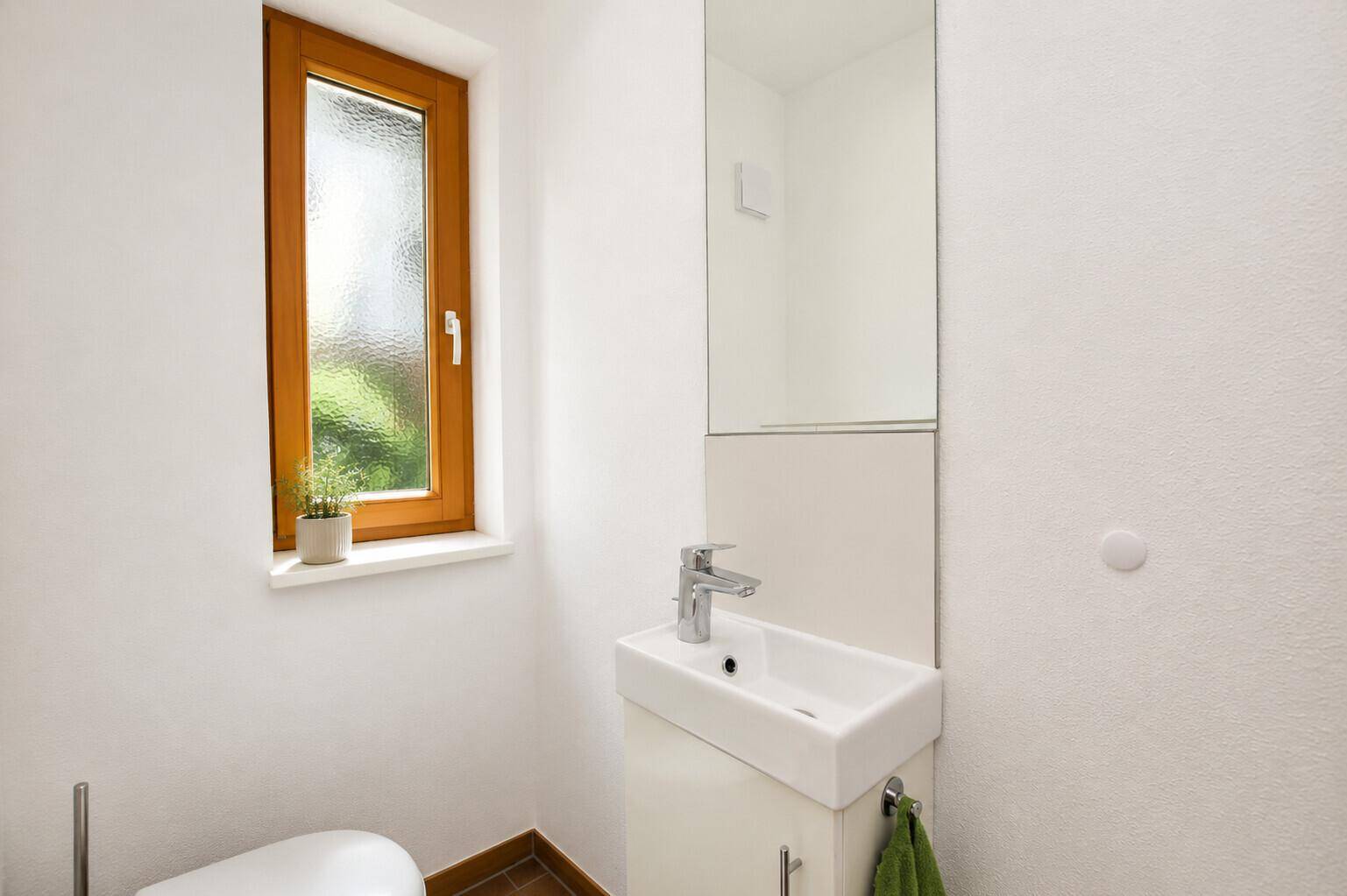 Modernes Gäste-WC mit Fenster, kleinem Waschbecken und Spiegel.