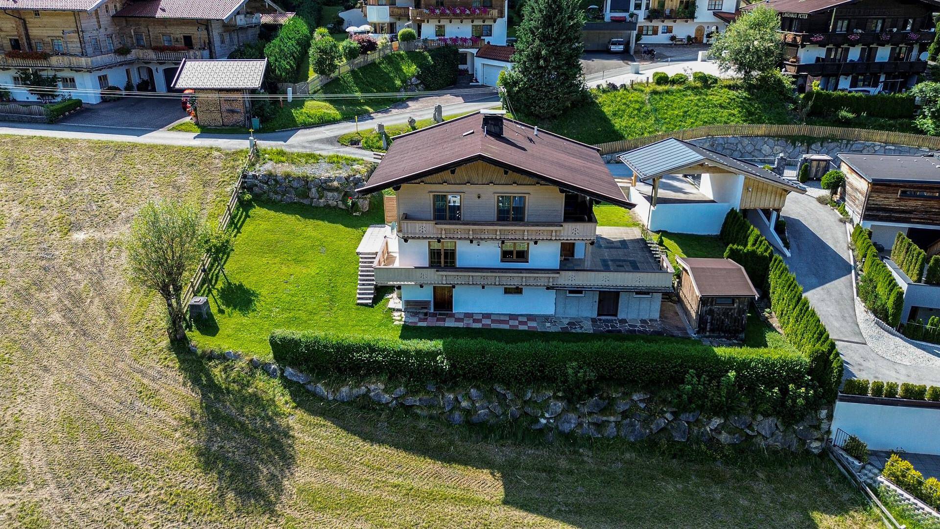 Luftaufnahme eines Wohnhauses mit gepflegtem Garten, umgeben von weiteren Häusern und Naturlandschaft.