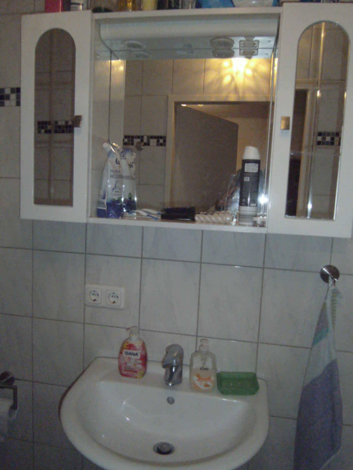 Badezimmer mit Waschbecken, Spiegelschrank und hellen Wandfliesen im klassischen Stil.