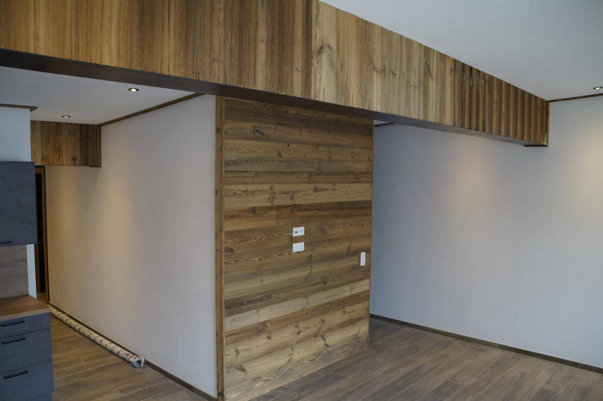 Offener Wohnbereich mit markanten Holzverkleidungen an Wänden und Decke, die eine warme Atmosphäre schaffen.
