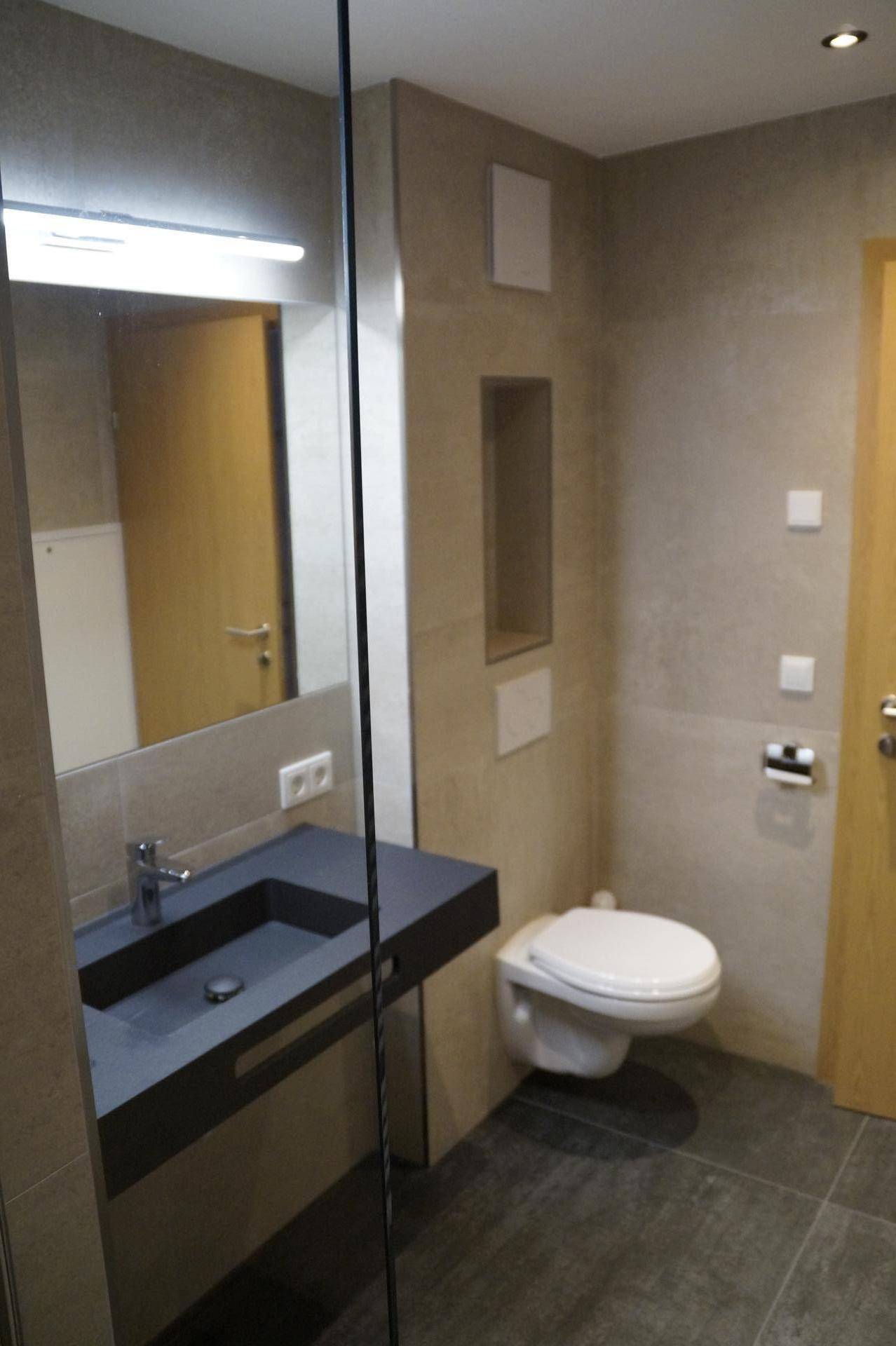 Modernes Badezimmer mit schwebendem Waschtisch, wandhängendem WC und großformatigen Fliesen in Beige- und Grautönen.