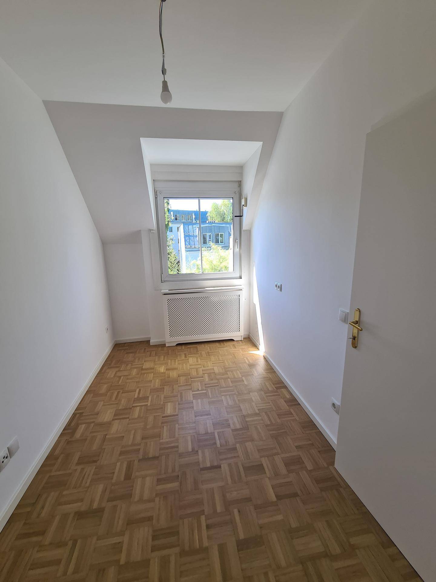 Helles Schlafzimmer mit Dachschräge, Parkettboden und Fenster.