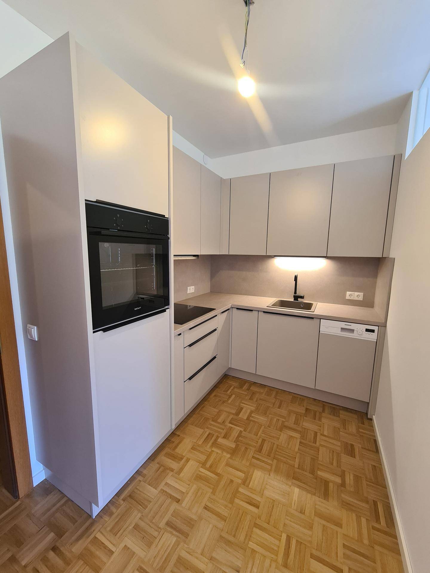 Moderne Einbauküche mit hellen Fronten, integriertem Backofen und Parkettboden.