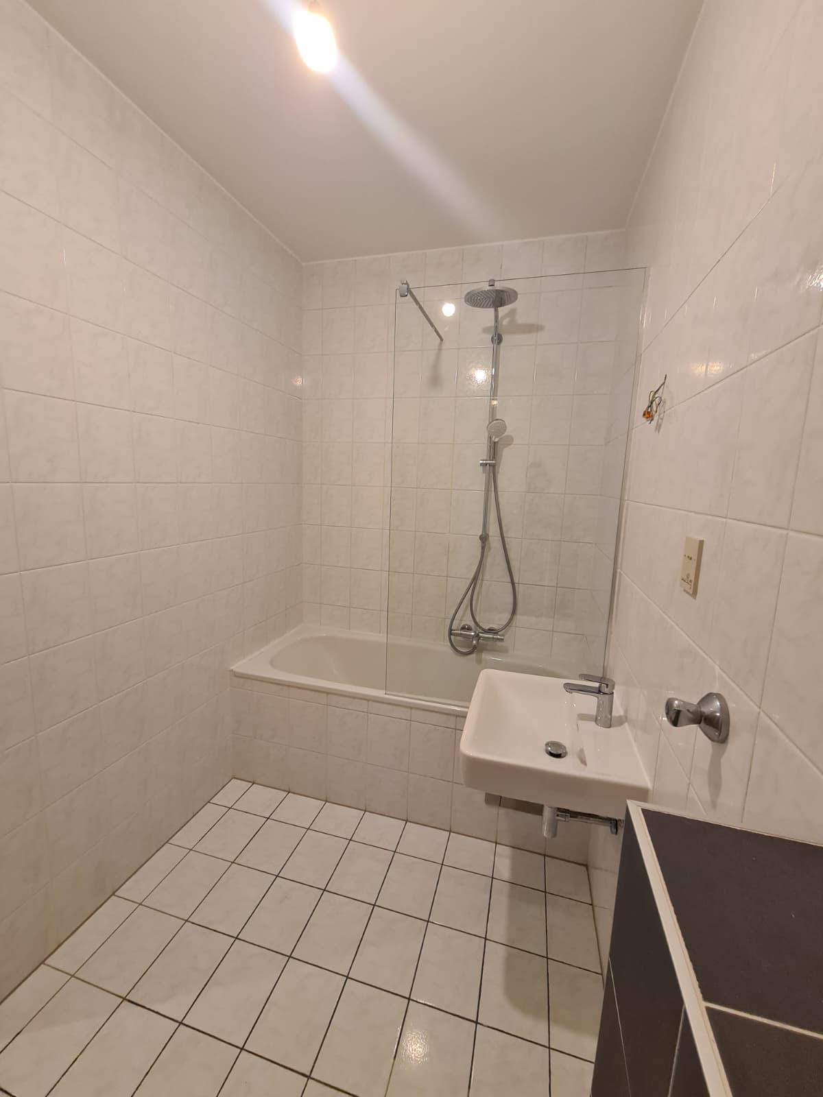 Helles Badezimmer mit Badewanne, Duschvorrichtung und weiß gefliesten Wänden.