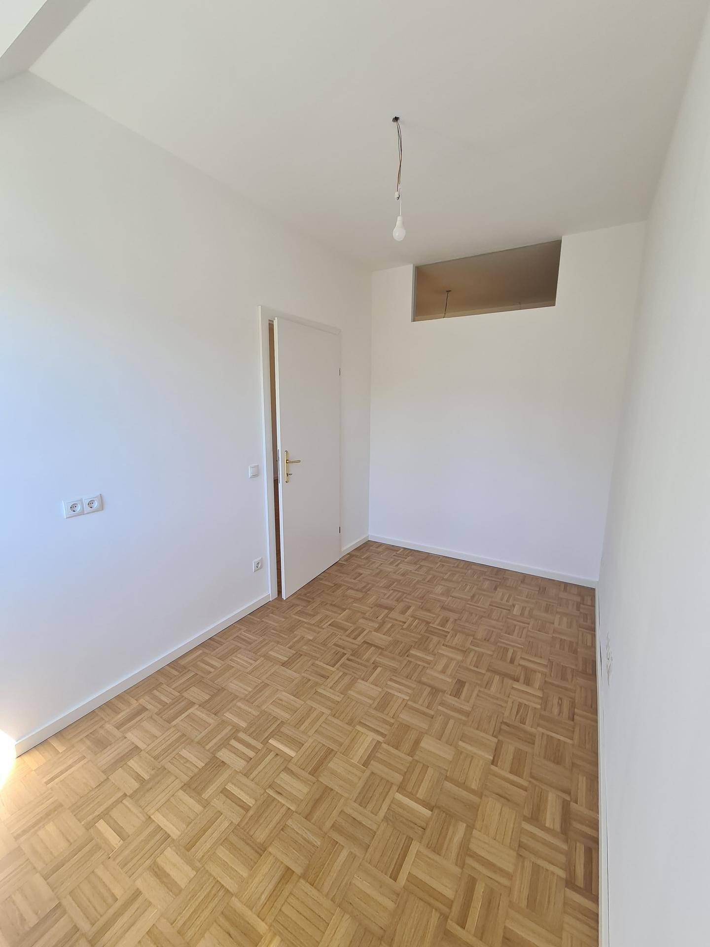 Leerer Raum mit Parkettboden und einer Tür, die zu weiteren Räumen führt.