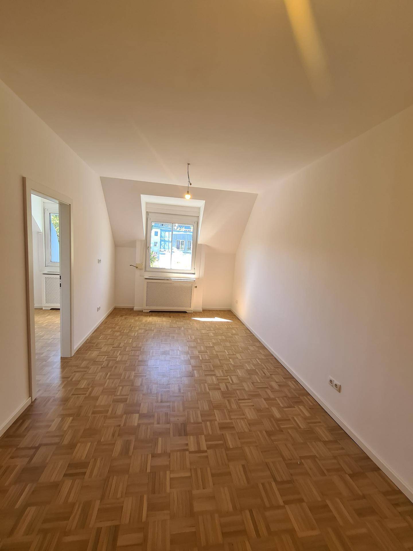 Geräumiger Wohnbereich mit Parkettboden, Dachschräge und hellem Fenster.