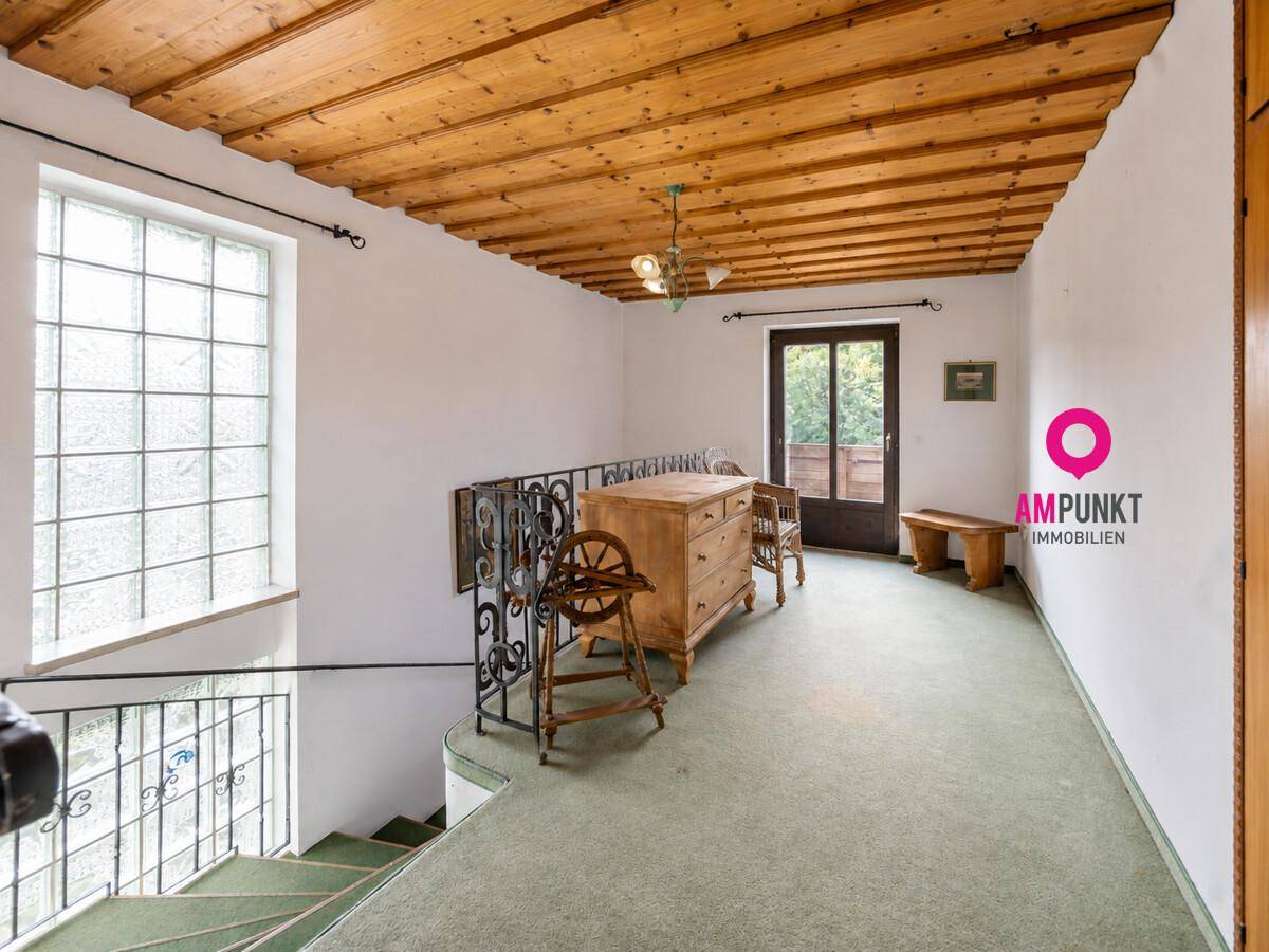 Obergeschoss-Flur mit Holzdecke, Teppichboden und Treppe mit schmiedeeisernem Geländer.