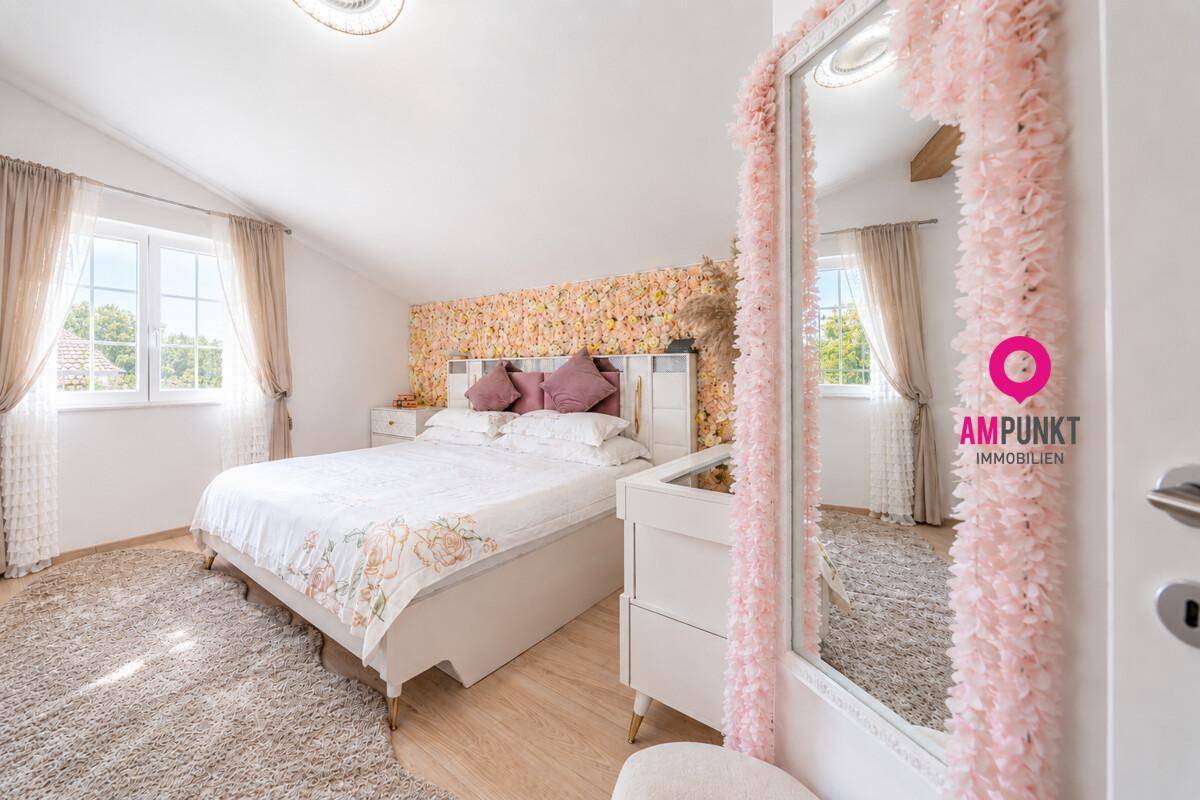 Geräumiges Schlafzimmer mit Dachschräge, Holzboden und floraler Wandgestaltung, sehr hell.