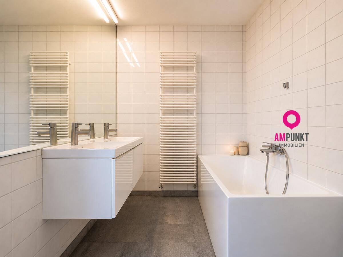 Helles Badezimmer mit Badewanne, Doppelwaschbecken und beheiztem Handtuchhalter.