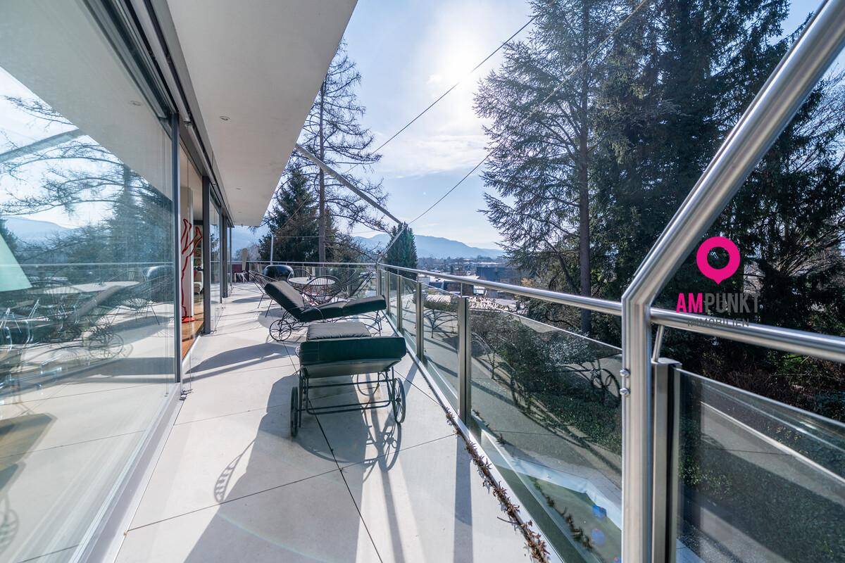 Langer Balkon mit Glasgeländer, Liegestühlen und weitem Blick ins Grüne.