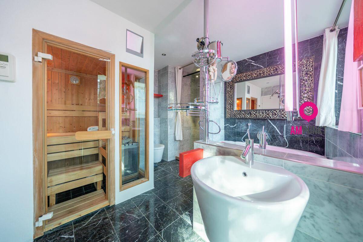 Luxuriöses Badezimmer mit integrierter Sauna, freistehendem Waschbecken und dunklen Marmorfliesen.