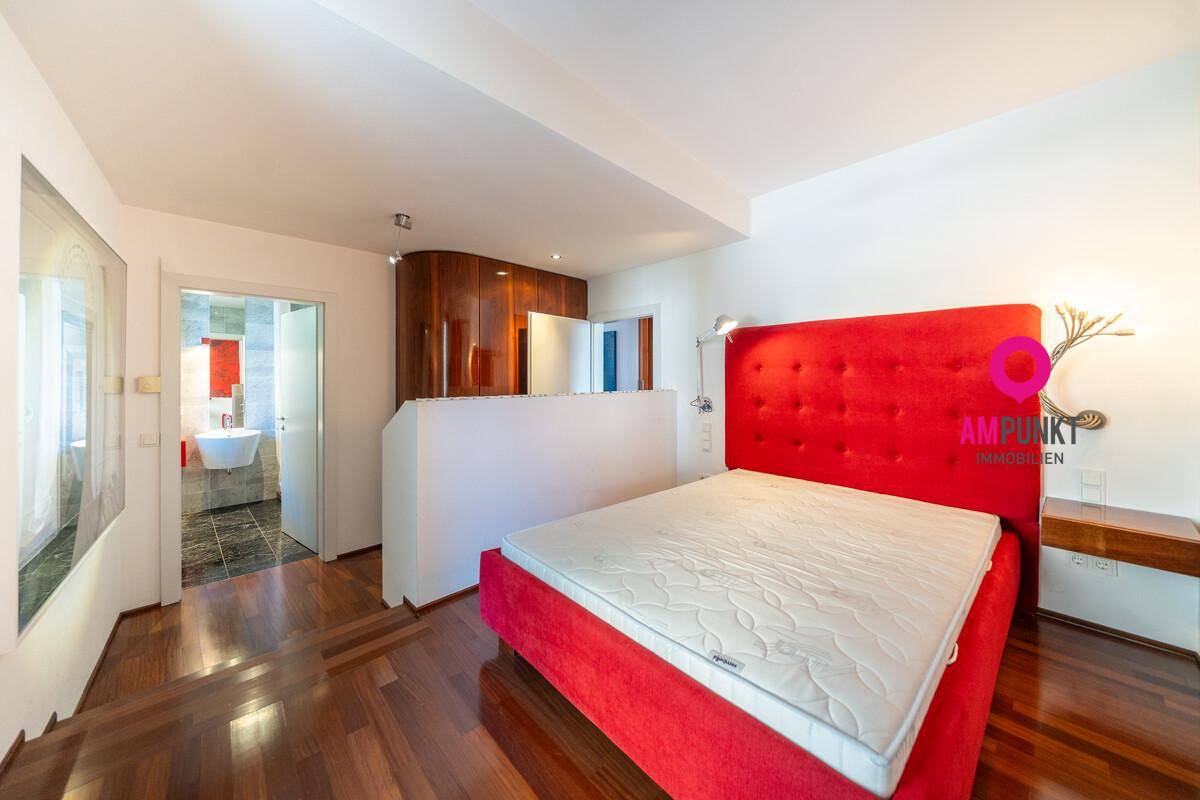 Schlafzimmer mit rotem Bett, Holzboden und direktem Zugang zu einem modernen Badezimmer.
