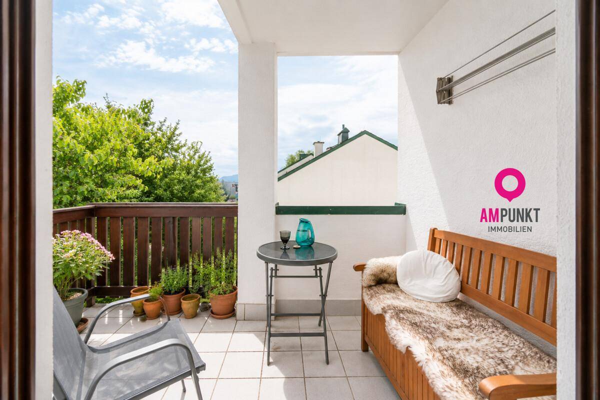 Sonniger Balkon mit Fliesenboden, Holzbänken und Blick auf die grüne Umgebung.