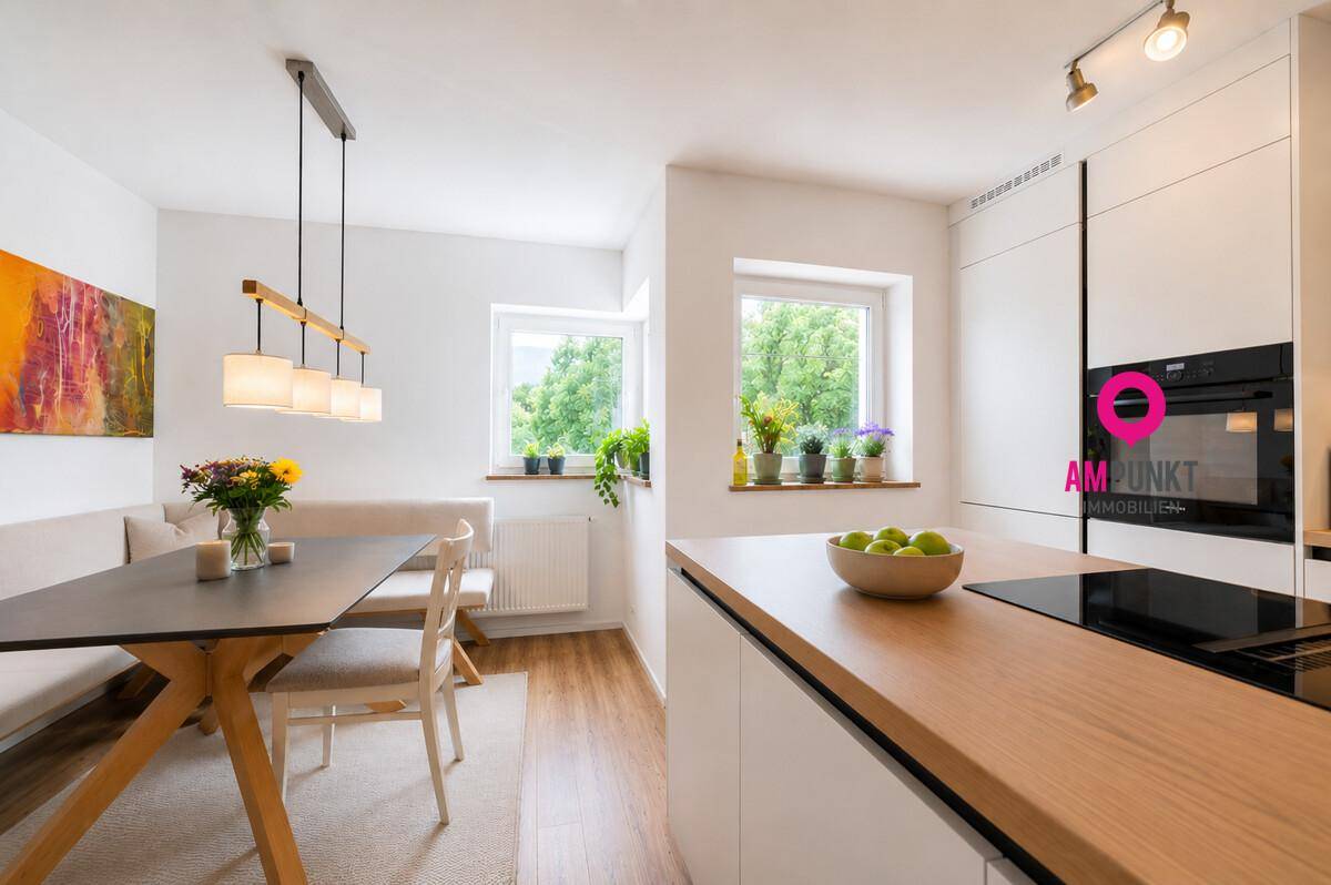 Helle, moderne Küche mit Essbereich, Holzarbeitsplatte und Blick ins Grüne durch große Fenster.