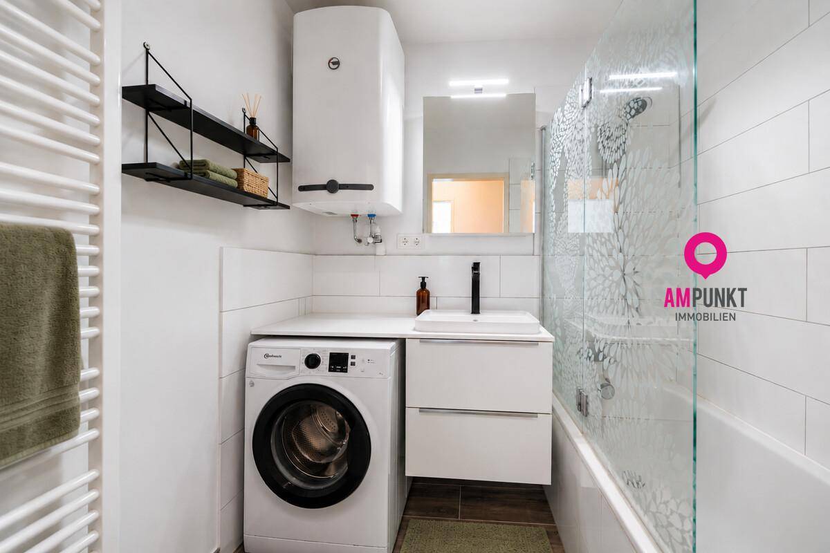 Modernes Badezimmer mit Waschmaschine, Waschbecken, Spiegelschrank und Duschbadewanne.