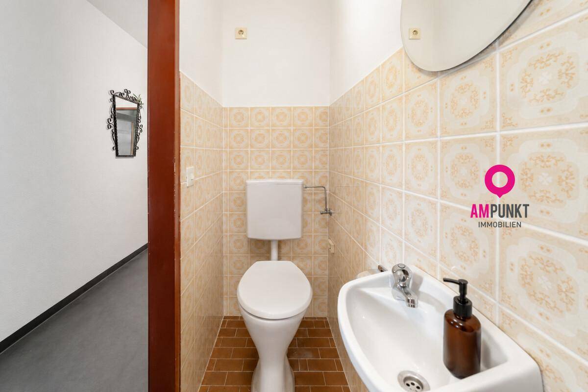 Kleines Gäste-WC mit beigefarbenen Fliesen, Toilette und Handwaschbecken.