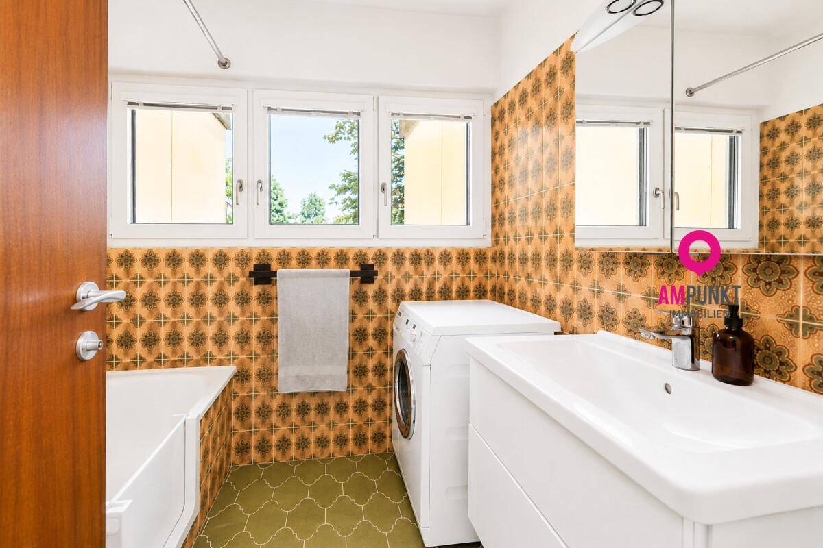 Badezimmer im 80er-Jahre-Stil mit gemusterten Fliesen, Badewanne und großem Fenster.