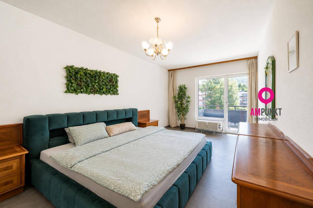 Geräumiges Schlafzimmer mit Balkonzugang, grüner Wanddekoration und Blick ins Grüne.