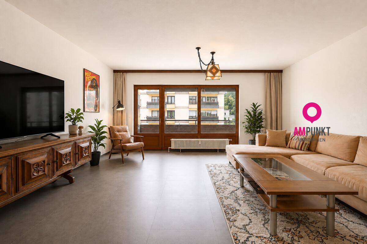 Geräumiges Wohnzimmer mit Zugang zum Balkon, beigem Sofa und traditionellem Holzmöbel.