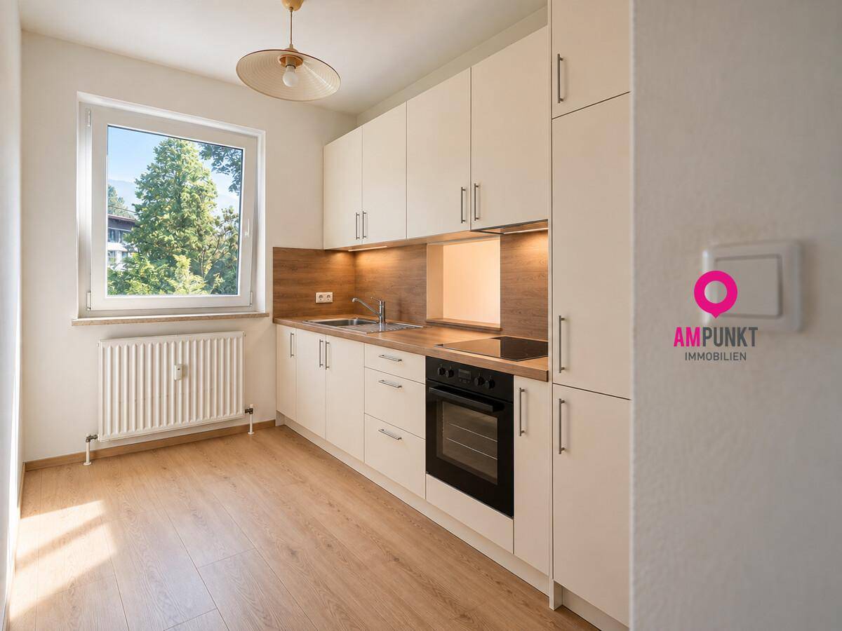 Funktionale Küche mit hellen Schränken, Holzarbeitsplatte und Fenster mit Blick ins Grüne.