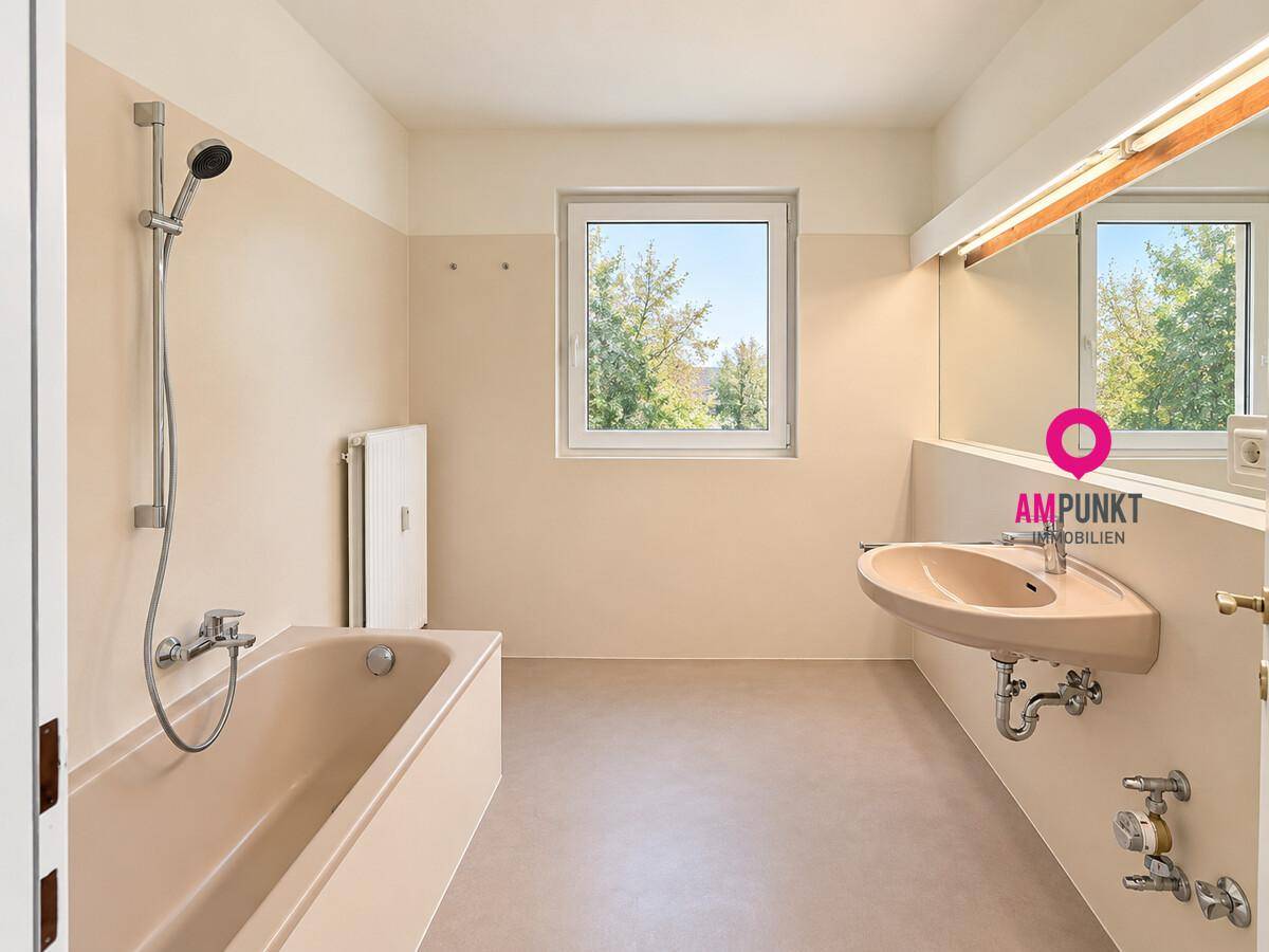 Badezimmer mit Badewanne, Waschbecken, Spiegel und Fenster, in einem älteren Stil gehalten.