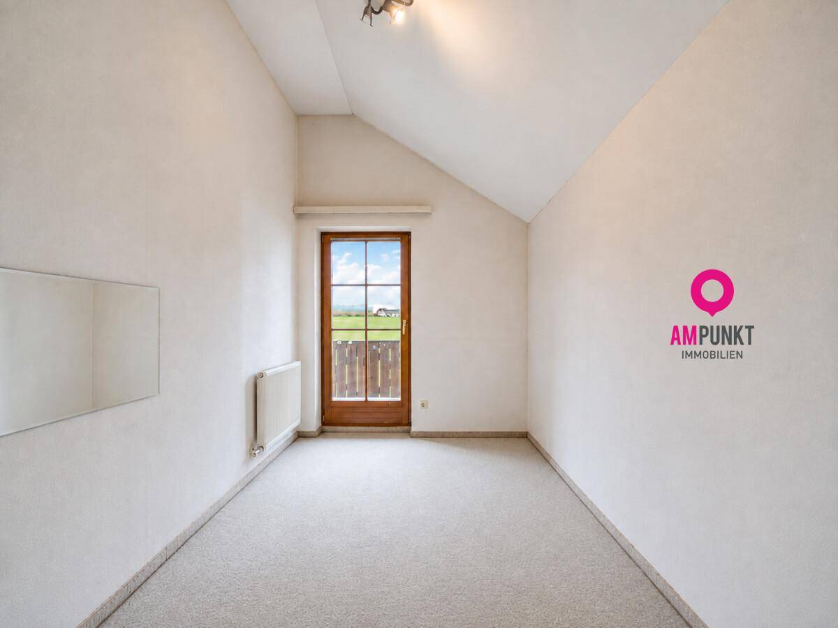 Helles Schlafzimmer mit Teppichboden, Dachschräge und Zugang zu einem französischen Balkon.