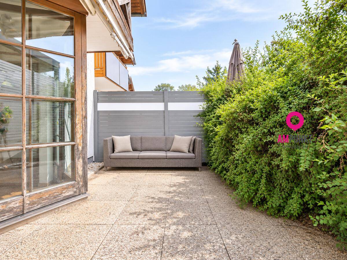 Sonniger Terrassenbereich mit Outdoor-Sofa und umgebender Hecke für Privatsphäre.