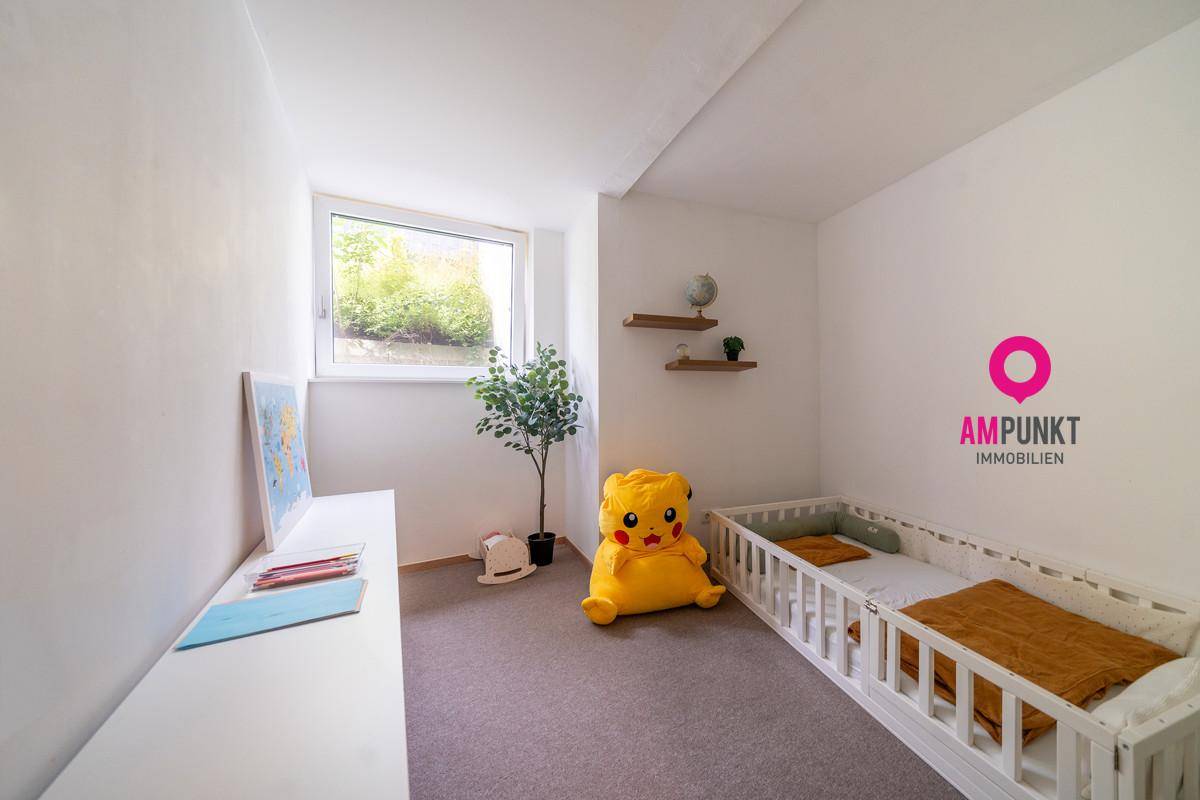 Helles Kinderzimmer mit großem Fenster, Teppichboden und einfacher, kindgerechter Einrichtung.