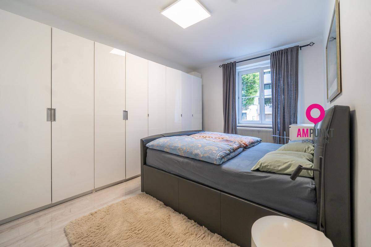 Helles Schlafzimmer mit großem Bett, glänzenden weißen Einbauschränken und Fenster.
