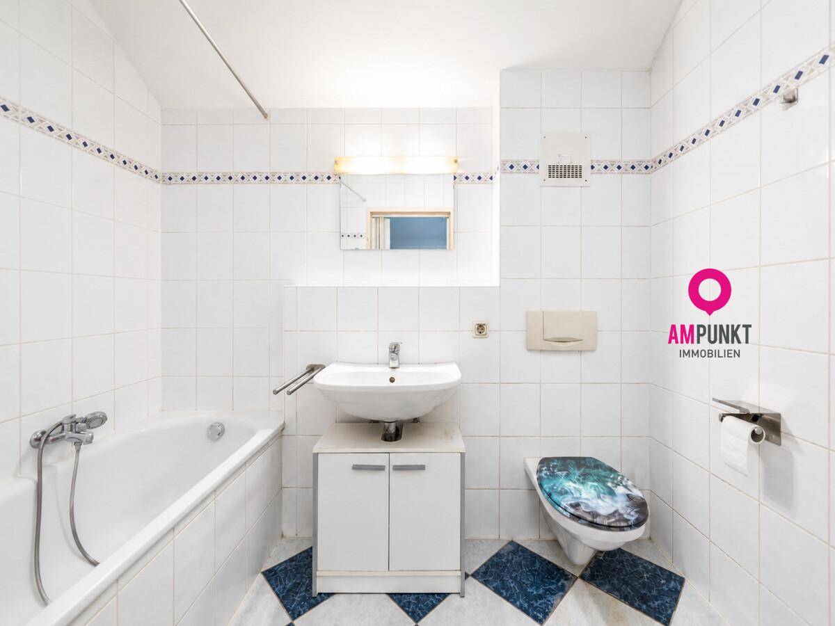Gefliestes Badezimmer mit Badewanne, Waschbecken und WC in weiß-blauem Design.