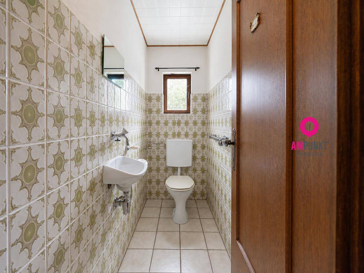 Kleines WC mit gemusterten Fliesen, Fenster und Wandgriff für Barrierefreiheit.