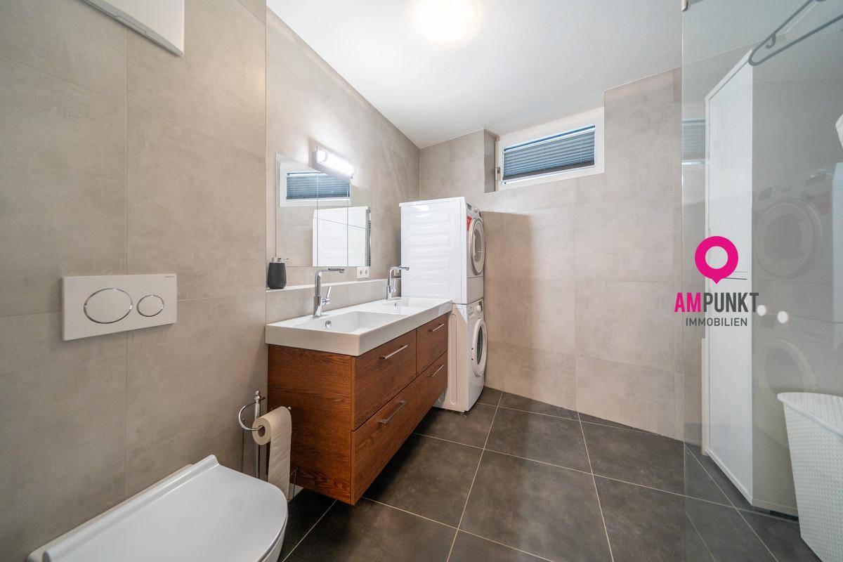 Geräumiges Badezimmer mit Doppelwaschbecken, Dusche und integriertem Waschmaschinenbereich.