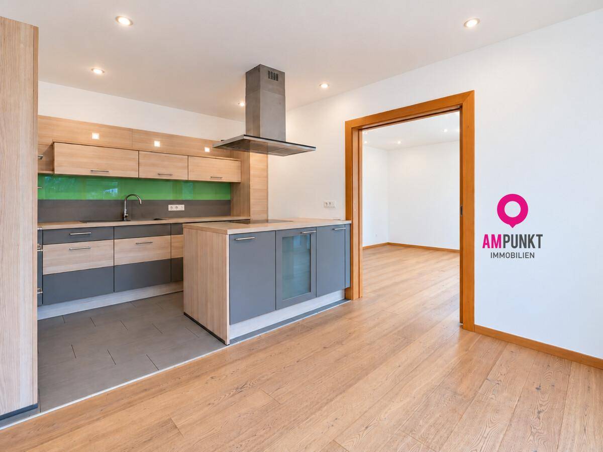 Moderne Einbauküche mit Kücheninsel, Holz- und Grautönen sowie grünem Spritzschutz.