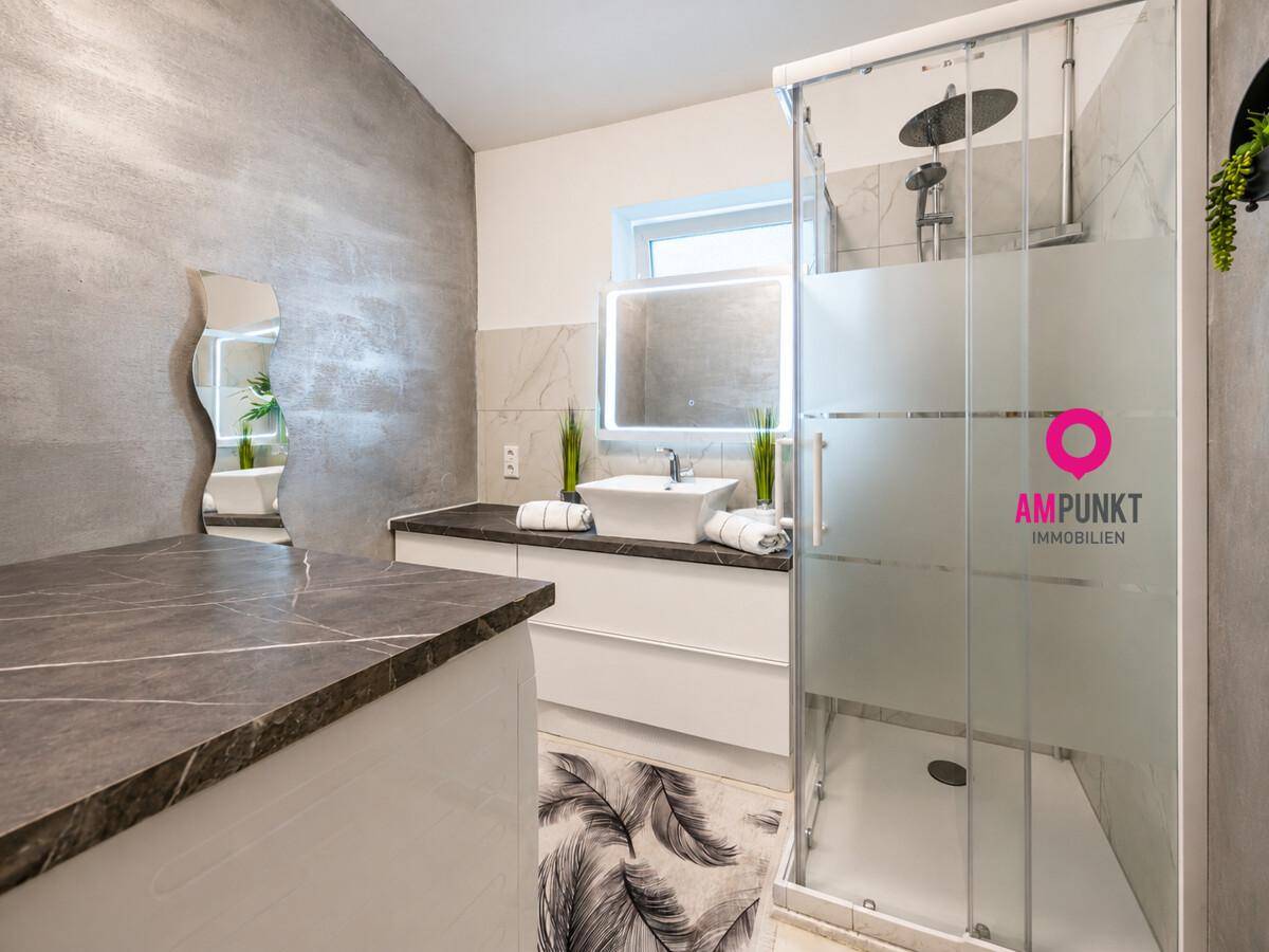 Modernes Badezimmer mit begehbarer Dusche, großformatigen Fliesen und beleuchtetem Spiegel.