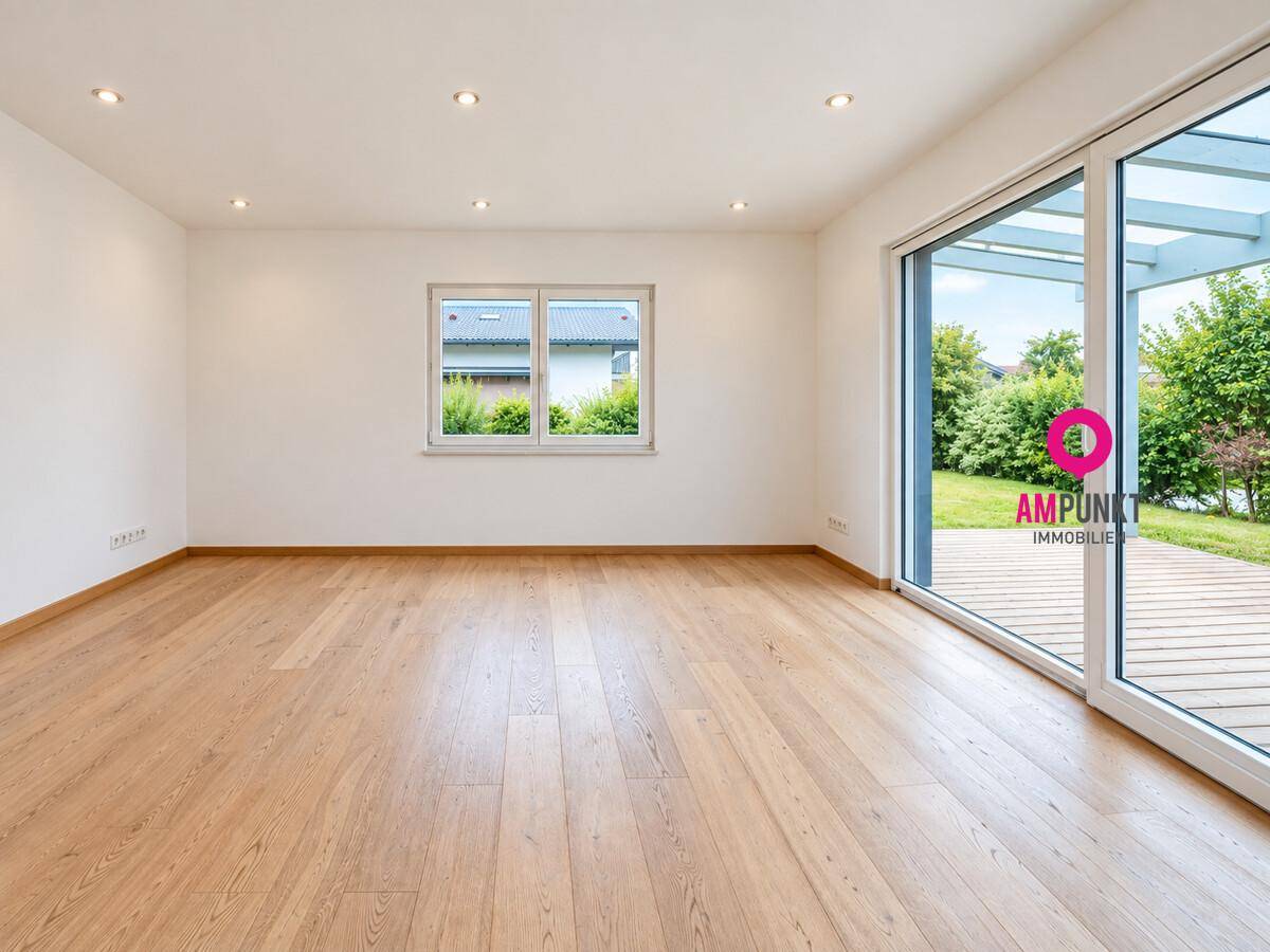 Helles Wohnzimmer mit Holzboden, großen Fenstern und direktem Zugang zur Holzterrasse und Garten.