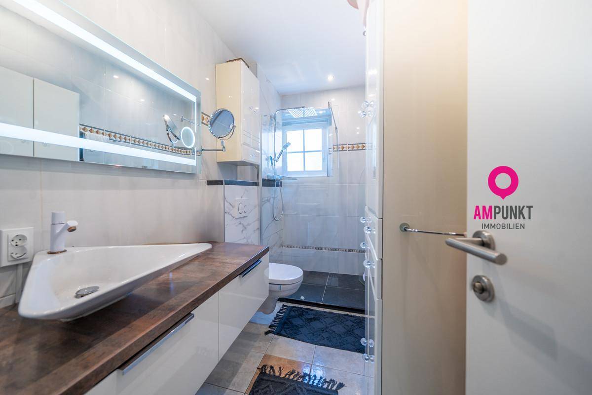 Modernes Badezimmer mit stilvollem Waschbecken, beleuchtetem Spiegel und Duschbereich.