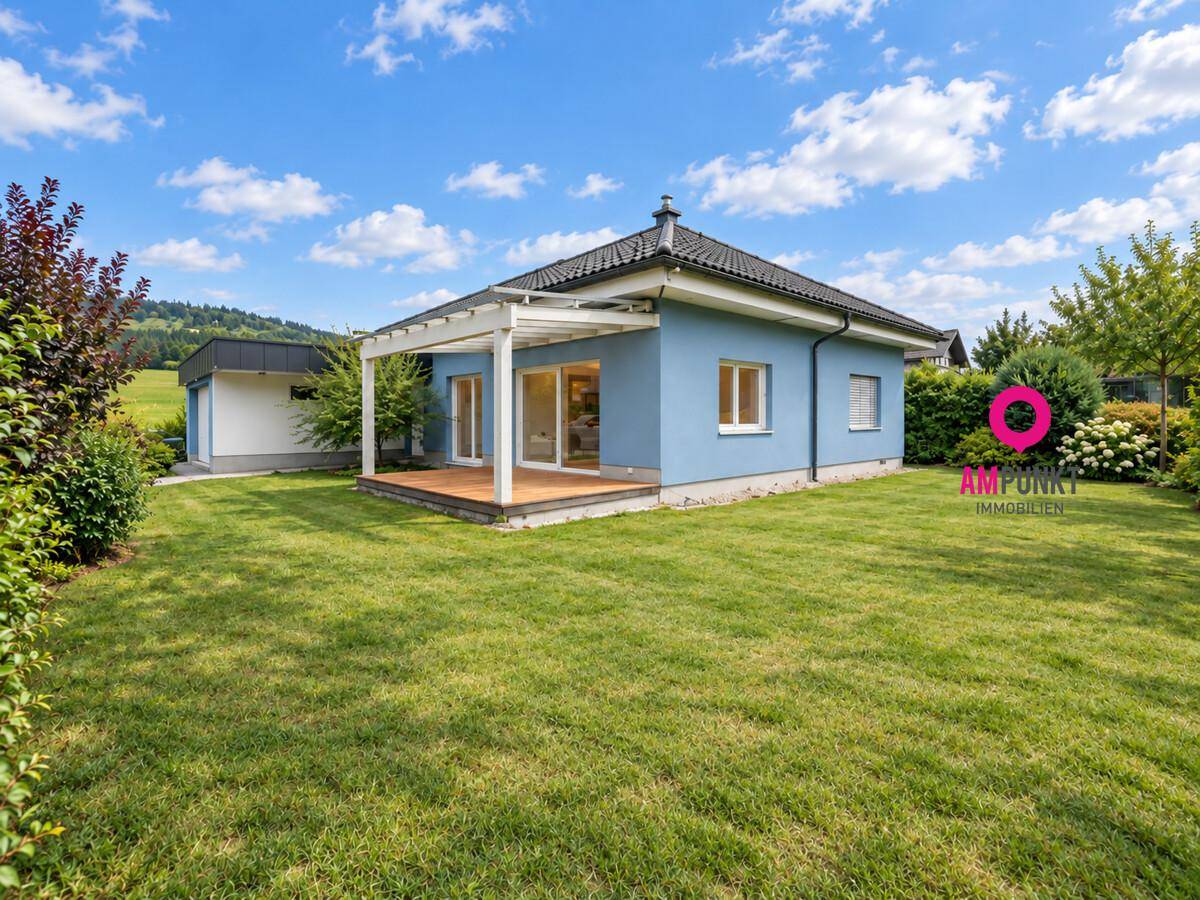 Charmantes blaues Haus mit Holzterrasse unter einer Pergola, umgeben von einem gepflegten Garten.
