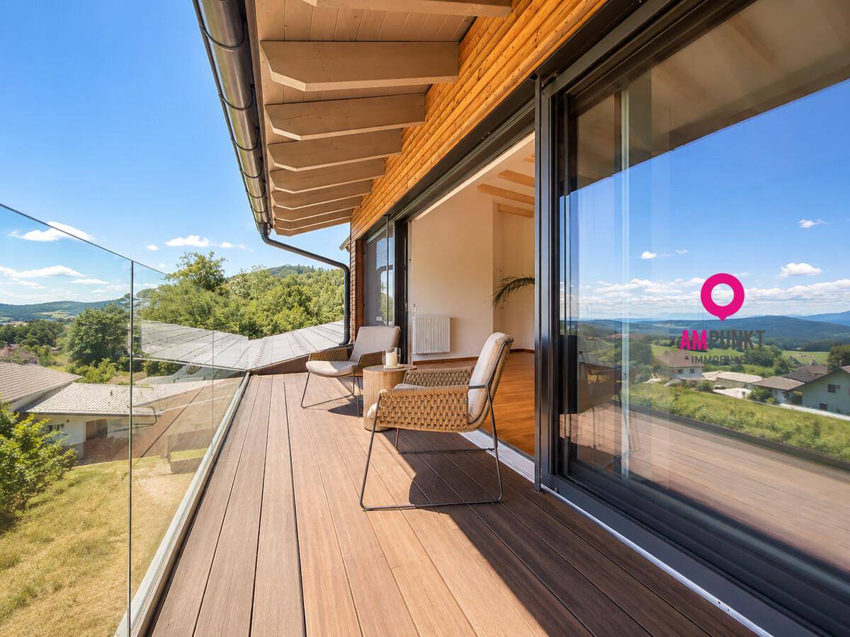 Geräumiger Balkon mit Glasgeländer, Holzboden und weitem Blick auf die Landschaft.