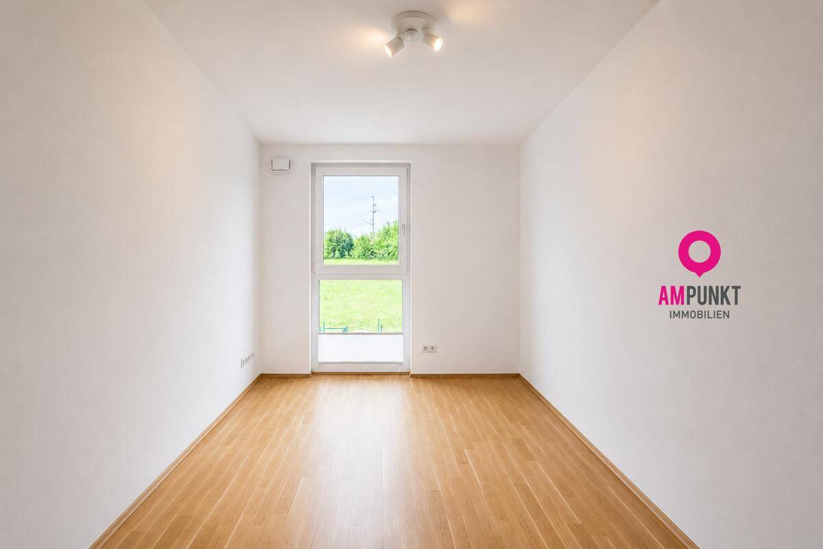 Leeres, helles Zimmer mit Holzboden und großem Fenster, vielseitig nutzbar als Schlaf- oder Arbeitszimmer.