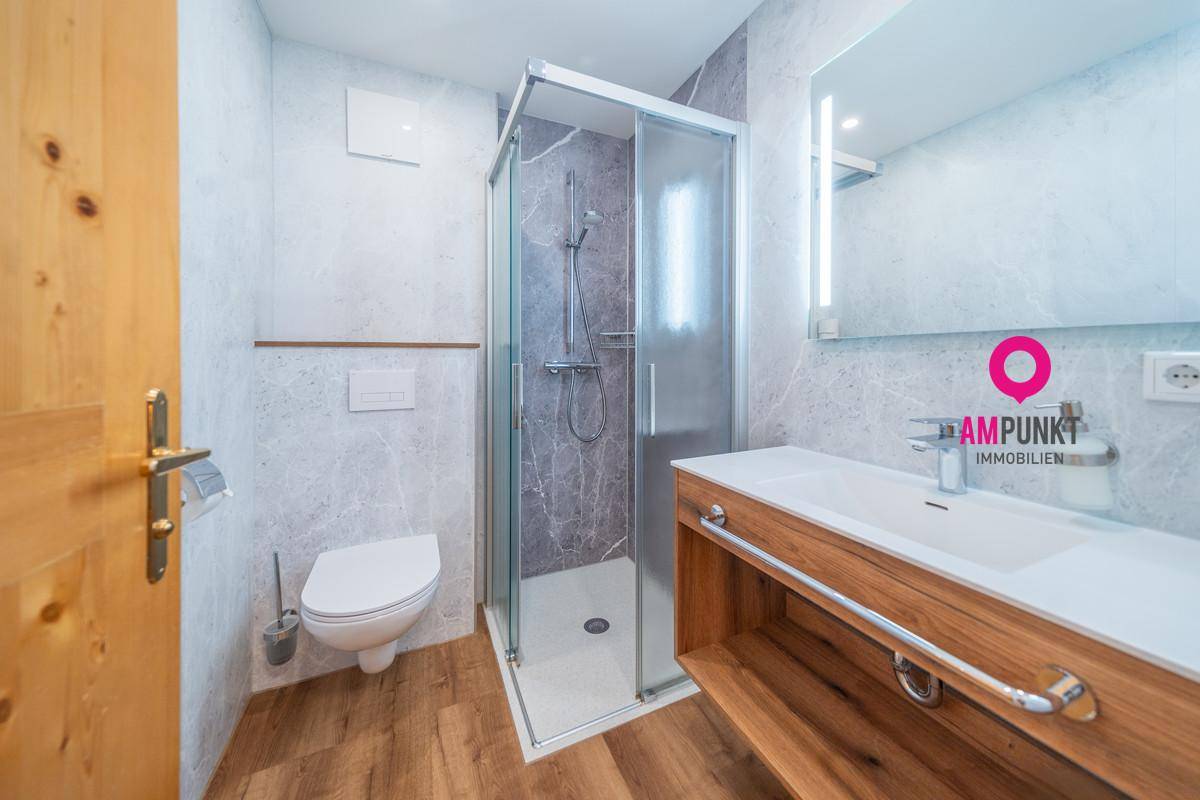 Modernes Badezimmer mit Duschkabine, WC, Waschbecken und Holzunterschrank, ausgestattet mit Fliesen und Holzboden.
