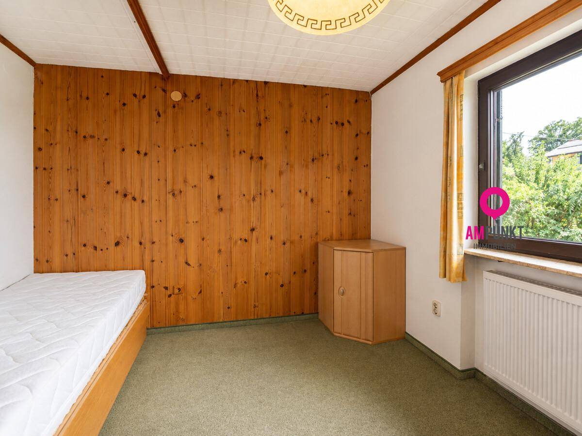 Schlafzimmer mit Holzvertäfelung, Teppichboden und Fenster mit Blick ins Grüne.