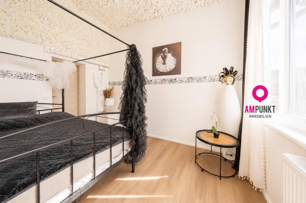 Helles Schlafzimmer mit Himmelbett und Holzboden, dekoriert mit floralen Akzenten.