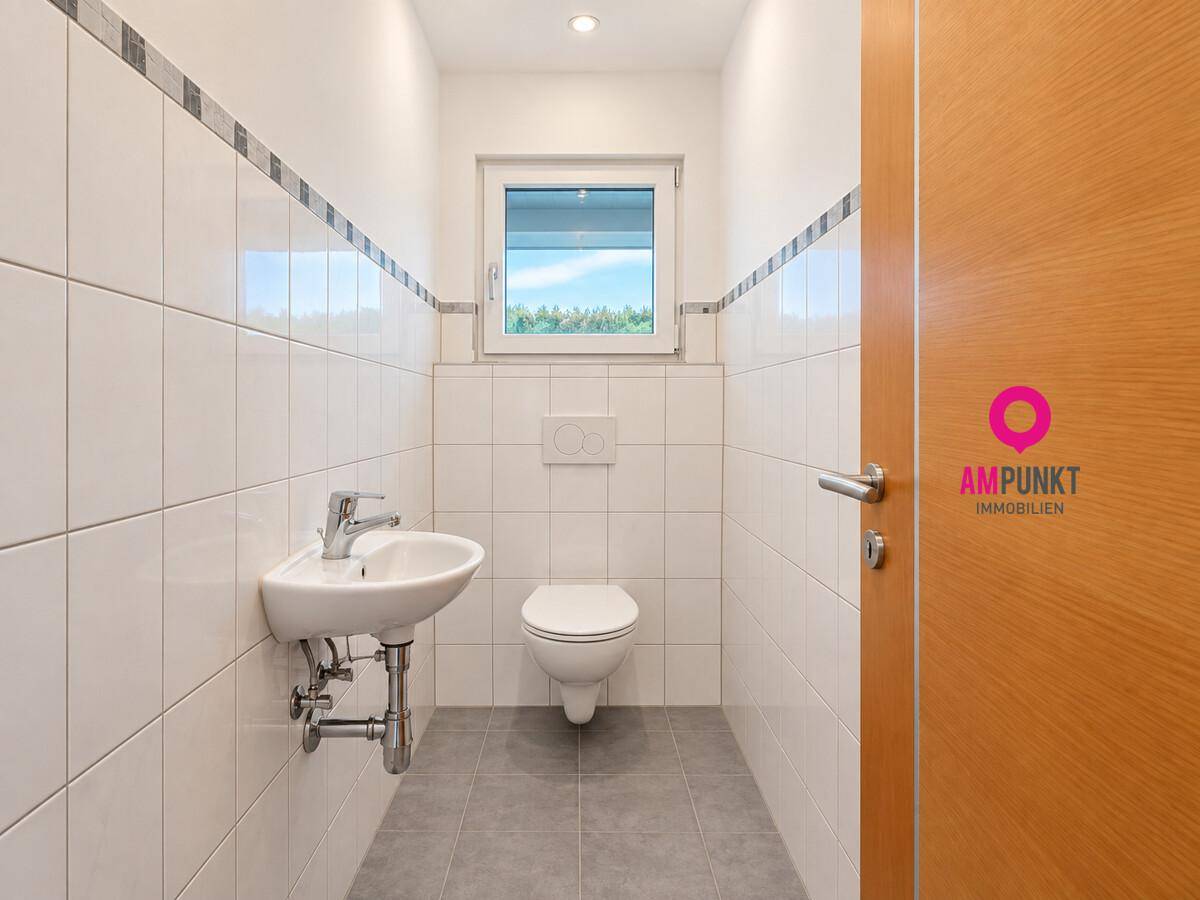 Gäste-WC mit wandhängender Toilette, kleinem Waschbecken und Fenster, hell gefliest.