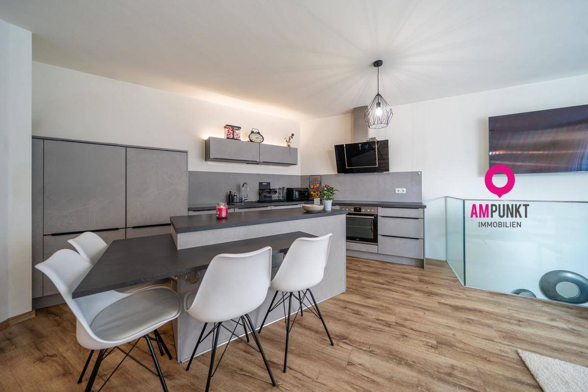 Moderne Einbauküche in Grau mit Kochinsel und Essbereich, ausgestattet mit hochwertigen Geräten.