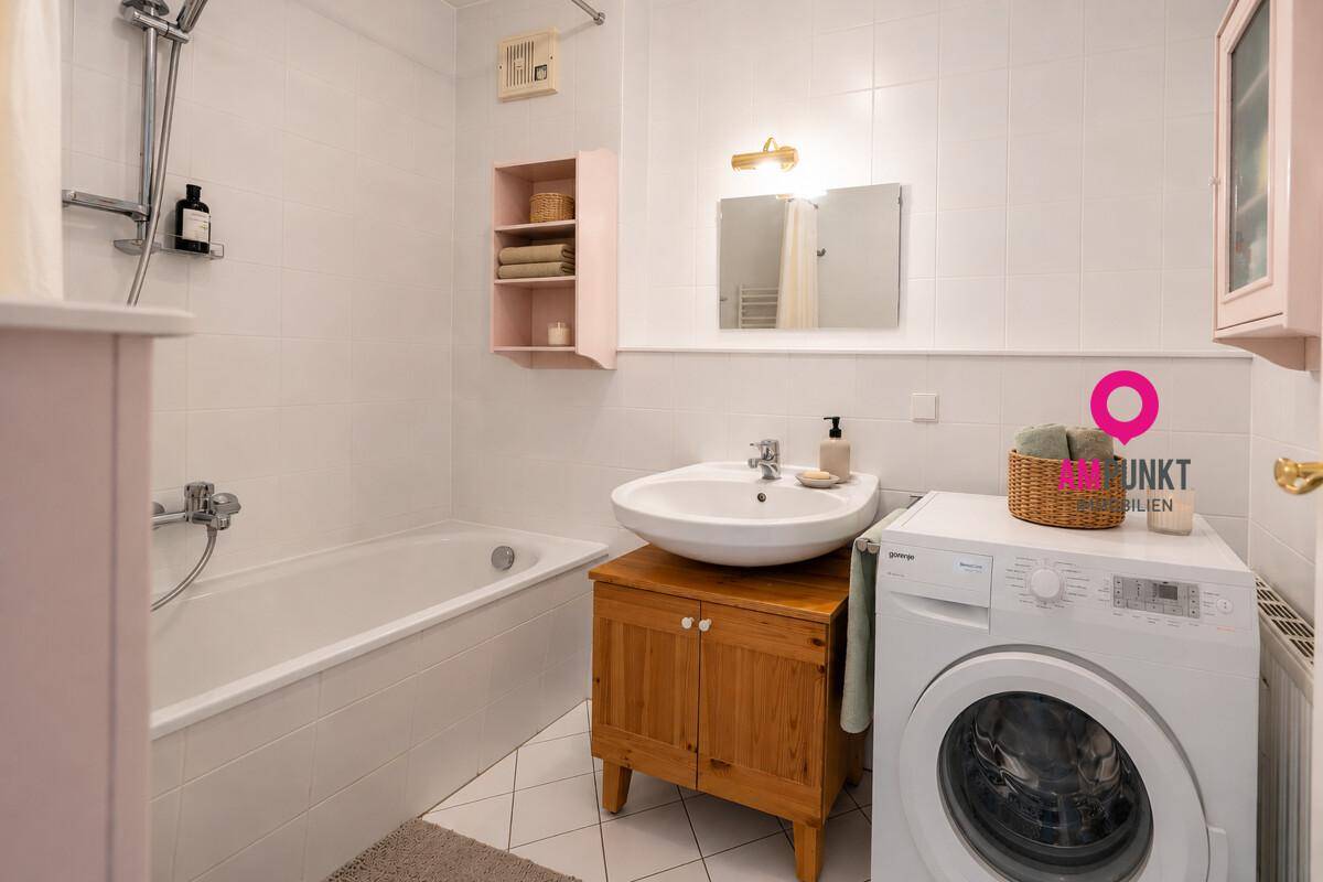 Funktionales Badezimmer mit Badewanne, Waschbecken und Waschmaschine, hell gefliest.