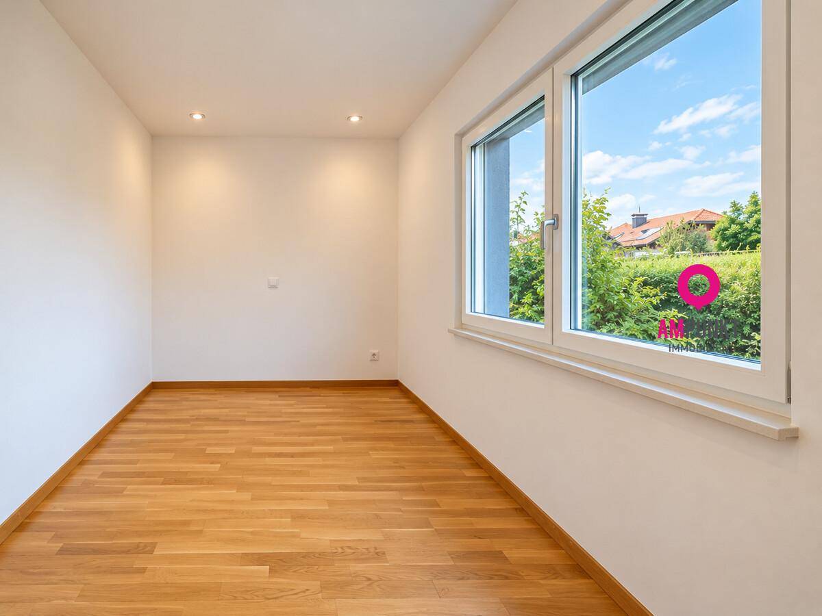 Freundliches Zimmer mit Holzboden und großem Fenster, das viel Tageslicht hereinlässt.