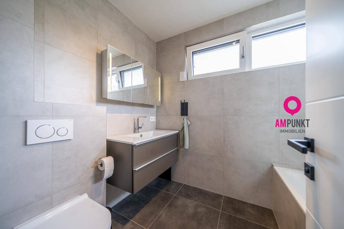 Modernes Badezimmer mit grauen Fliesen, wandhängendem WC und Waschtischunterschrank.