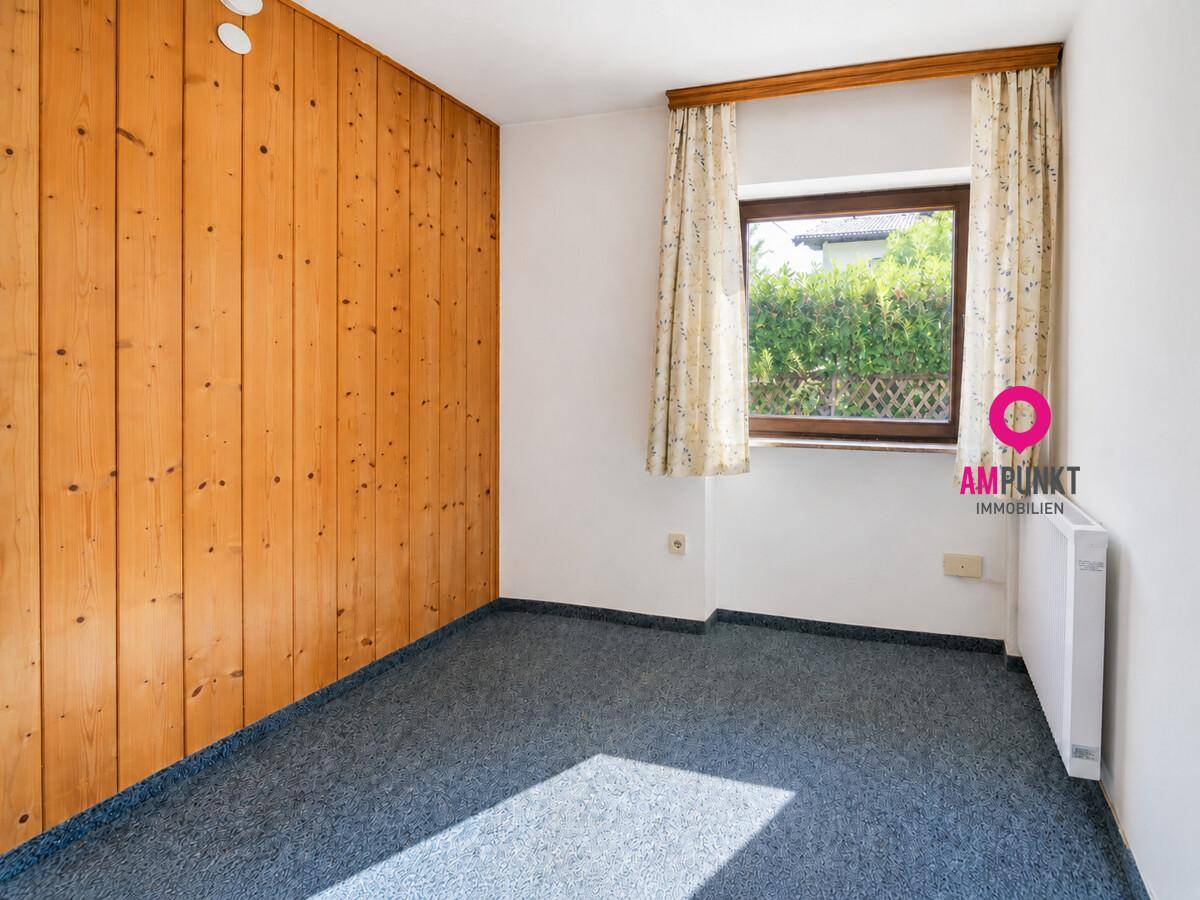 Schlafzimmer mit Holzvertäfelung, Teppichboden und Blick ins Grüne.