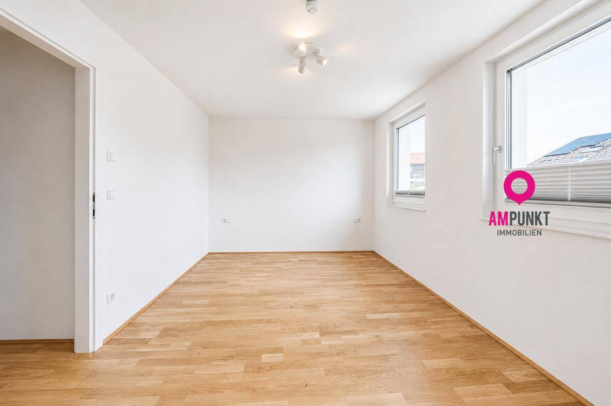 Leeres, helles Zimmer mit Holzboden und großen Fenstern, vielseitig nutzbar als Schlaf- oder Arbeitszimmer.