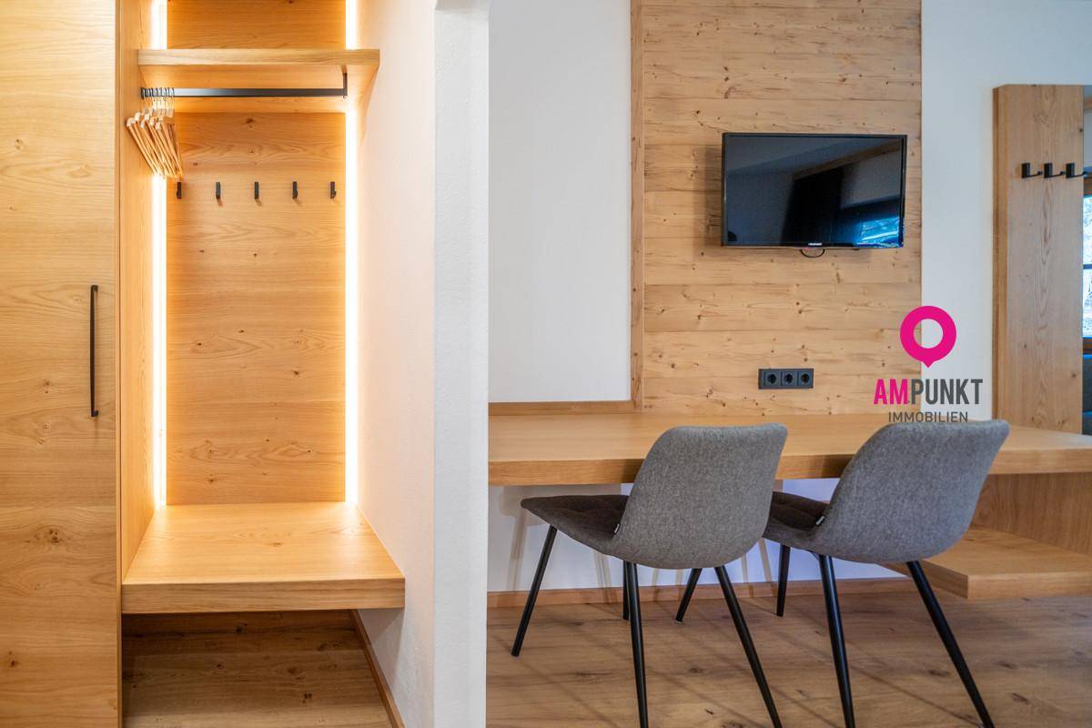 Moderner Schreibtischbereich mit zwei Stühlen und integriertem Kleiderschrank in Holzoptik, gut beleuchtet.